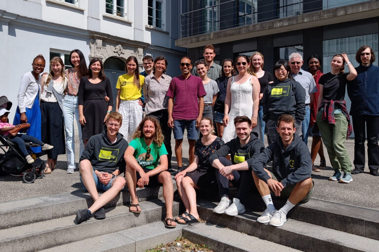 Auf dem Bild sind die Teammitglieder auf der Integreat-Konferenz zu sehen, die vor der Hochschule Augsburg in der Sonne stehen.